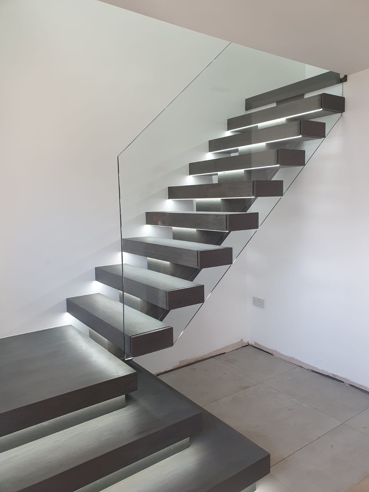 A floating staircase in black with glass panels and under stair lighting